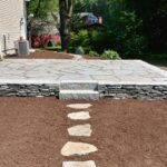 New mulching, irregular bluestone patio, chipped stone wall, and natural stone steppers by Riverfront Landscaping